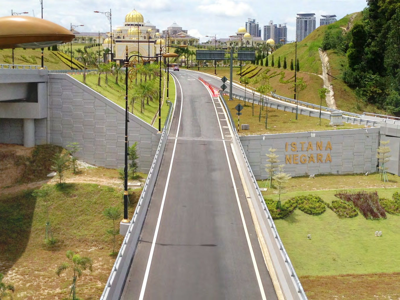 Istana Negara approach road with AnchorSOL retaining wall carrying carved 'ISTANA NEGARA' signage, National Palace in the background